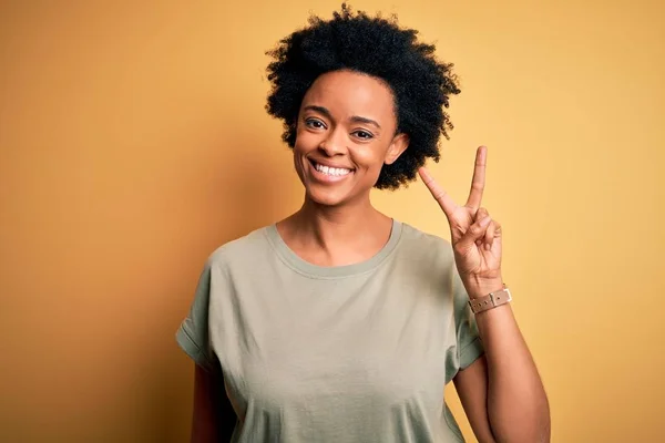若いです美しいですアフリカ系アメリカ人アフロ女性とともに巻き毛を身に着けていますカジュアルなTシャツショーや指数2で指摘しながら 自信と幸せ — ストック写真