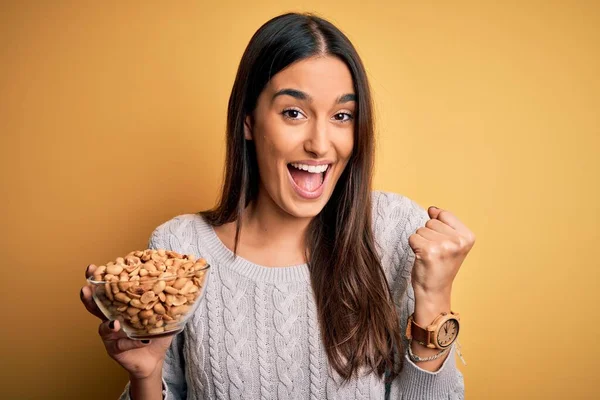 Young Beautiful Brunette Woman Holding Bowl Peanuts Isolated Yellow Background — 스톡 사진