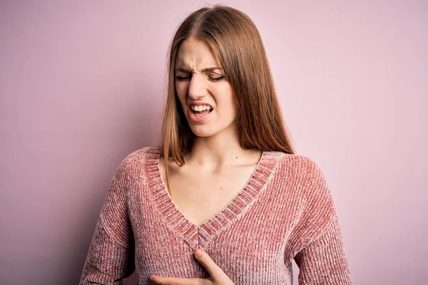若い美しい赤毛の女性が胃の上に手で孤立したピンクの背景にカジュアルなセーターを着て吐き気 痛みを伴う病気が体調を崩します アチェの概念 — ストック写真