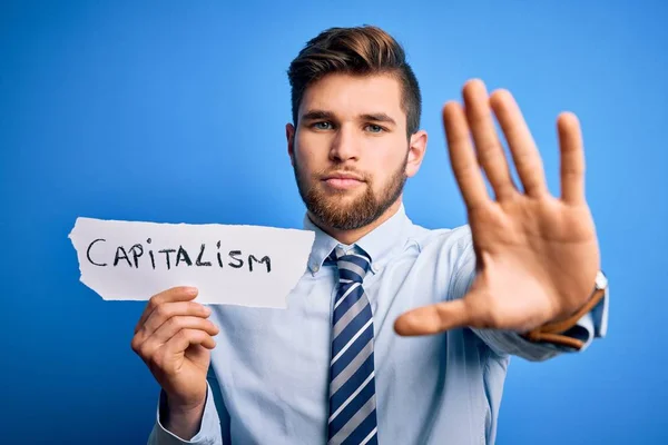 ひげと青い目を持つ若いブロンドのビジネスマンは 資本主義のメッセージで紙を保持します — ストック写真