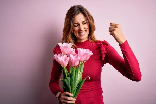 Young beautiful brunette woman holding bouquet of pink tulips over isolated background very happy and excited doing winner gesture with arms raised, smiling and screaming for success. Celebration concept. — Stock Image Young Beautiful Brunette Woman Holding Bouquet Pink Tulips Isolated Background Stock Image