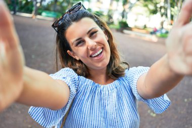 Yeşil Park 'ta mutlu ve neşeli gülümseyen güzel bir kadın güneşli bir yaz gününde akıllı telefon kullanarak selfie çekiyor.