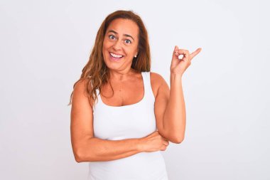 Middle age mature woman standing over white isolated background with a big smile on face, pointing with hand finger to the side looking at the camera.