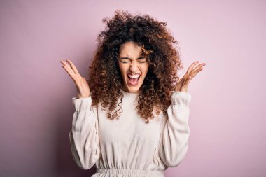 Kıvırcık saçlı ve piercingli güzel bir kadın pembe arka plan üzerine gündelik süveter giyerek başarının çılgınlığını kollarını kaldırarak ve gözlerini kapayarak heyecanla bağırarak kutluyor. Kazanan konsept