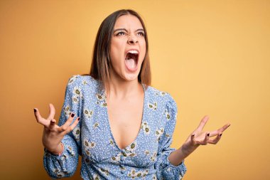 Genç, güzel, esmer, sıradan bir tişört giyen, sarı arka planda dikilen, deli deli deli bağıran, agresif ifade ve kollarıyla bağıran bir kadın. Hayal kırıklığı konsepti.