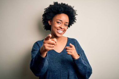 Kıvırcık saçlı, sıradan süveter giyen, mutlu ve komik yüzlü genç, güzel Afro-Amerikan kadın kamerayı işaret ediyor. İyi enerji ve titreşimler.