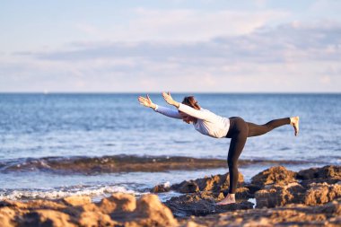 Genç yakışıklı sporcu yoga yapıyor. Koç kumsalda savaşçı pozu veriyor.