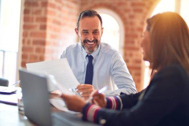 Mutlu ve kendinden emin gülümseyen iki orta yaşlı iş adamı. Ofiste dizüstü bilgisayarla gülümseyerek birlikte çalışıyoruz.