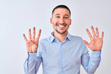 Genç yakışıklı iş adamı izole edilmiş arka planda durup dokuz numaralı parmaklarıyla işaret ederken kendinden emin ve mutlu bir şekilde gülümsüyor..