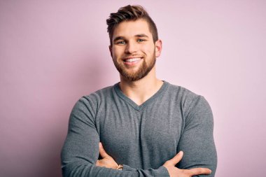 Sakallı, mavi gözlü, sıradan bir süveter giyen, kollarını kavuşturup kameraya gülümseyen yakışıklı sarışın genç bir adam. Pozitif kişi.