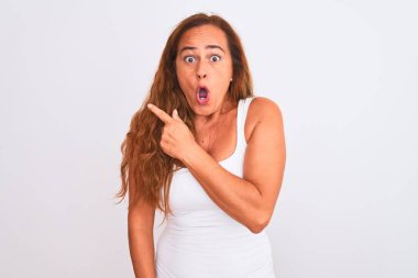 Middle age mature woman standing over white isolated background Surprised pointing with finger to the side, open mouth amazed expression.
