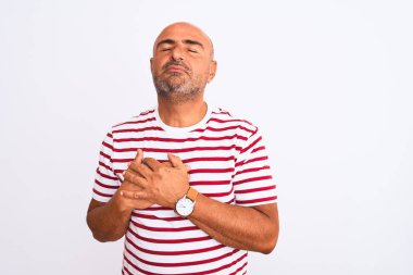 Middle age handsome man wearing striped t-shirt standing over isolated white background smiling with hands on chest with closed eyes and grateful gesture on face. Health concept.