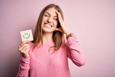Elinde gülümseyen emoji mesajıyla hatırlatma kağıdı tutan genç, güzel, kızıl saçlı bir kadın. Utanç ve şaşkınlık dolu, sinirli ve hayal kırıklığına uğramış bir yüz. Hata için korku ve üzüntü.