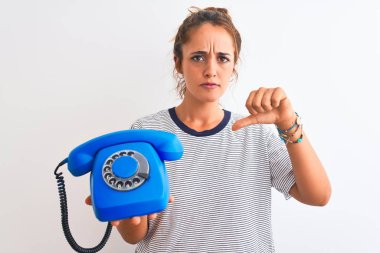 Genç, kızıl saçlı bir kadın klasik retro telefonu izole edilmiş arka planda tutuyor. Kızgın bir yüzü var. Eksi işareti var.