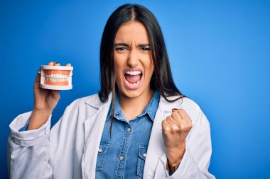 Plastik diş protezi tutan güzel, esmer dişçi kadın sinirlendi ve sinirlendi. Öfkeyle bağırdı.