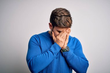 Young handsome blond man with beard and blue eyes wearing casual sweater with sad expression covering face with hands while crying. Depression concept.