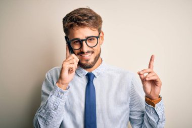 Genç işadamı beyaz arka planda akıllı telefondan konuşuyor. Bir fikir ya da soru işareti ile şaşırdı. Bir numara: