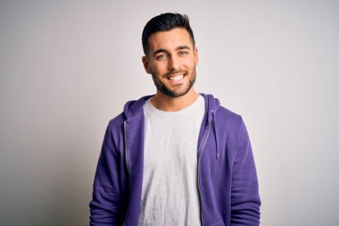 Young handsome man wearing purple sweatshirt standing over isolated white background with a happy and cool smile on face. Lucky person.