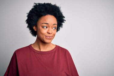 Kıvırcık saçlı, sıradan tişörtlü, gülümseyen ve gözlerini kaçıran güzel Afro-Amerikan kadın..