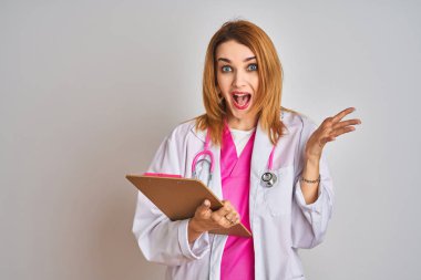 Kızıl saçlı, beyaz kadın, pembe steteskop takmış, elinde dosyayla çok mutlu ve heyecanlı, kazanan yüz ifadesi zaferi büyük bir gülümsemeyle kutluyor ve ellerini kaldırıyor.