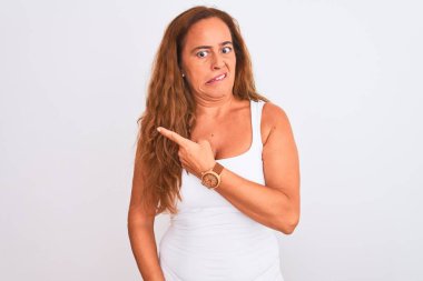 Orta yaşlı olgun bir kadın beyaz soyutlanmış arka planda dikiliyor. Endişeli ve endişeli bir ifadeye işaret ediyor.