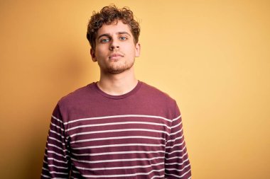 Sarışın, kıvırcık saçlı, sıradan çizgili süveter giyen, yüzünde ciddi bir ifade olan genç, yakışıklı bir adam. Basit ve doğal bir şekilde kameraya bakıyorsun..