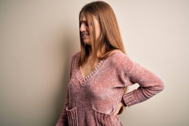 Genç, güzel, kızıl saçlı, pembe kazak giyen, izole edilmiş beyaz bir arka planı olan, sırt ağrısı çeken, elle dokunan, kas ağrısı çeken bir kadın.