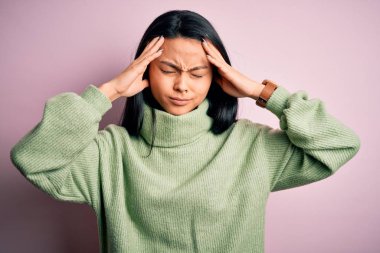 Genç ve güzel Çinli kadın balıkçı yaka kazak giyip izole edilmiş pembe arka planda acı ve migren yüzünden çaresiz ve stresli baş ağrısından muzdarip. Ellerini başının üstüne koy..