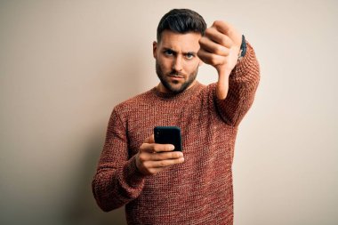 Young handsome man having conversation using smartphone over white background with angry face, negative sign showing dislike with thumbs down, rejection concept