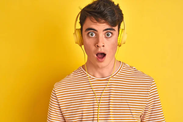 Teenager Chlapec Nosí Sluchátka Přes Izolované Žluté Pozadí Strach Šokován — Stock fotografie