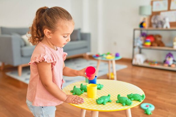 Beautiful blond toddler girl playing with plastic frogs toys at kindergarten