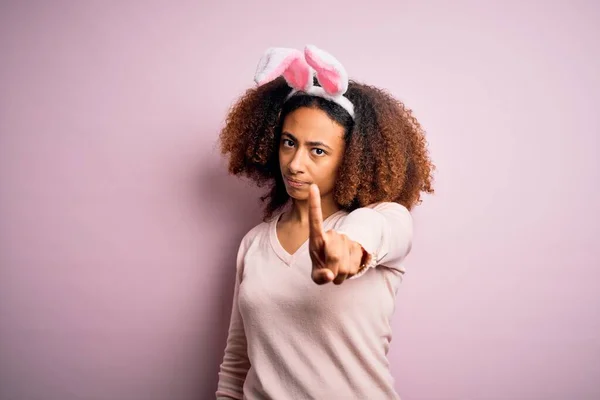一个年轻的非洲裔美国女人 一头黑发 红红的背景上戴着小兔子耳朵 带着手指尖尖着 满脸怒容 毫无表情 — 图库照片