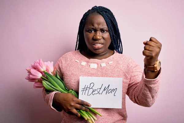 Plus size african american woman holding best mom message and tulips on mothers day annoyed and frustrated shouting with anger, crazy and yelling with raised hand, anger concept