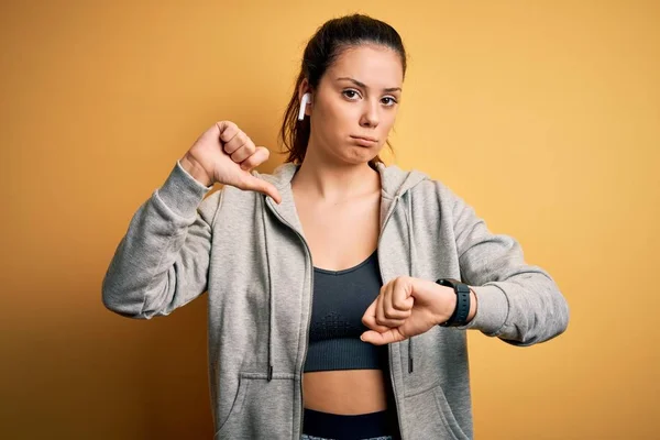 若い美しいブルネットのスポーツ女性は怒っている顔でスポーツをするイヤホンを使用して音楽を聴く 親指で嫌いを示す負のサインダウン 拒絶コンセプト — ストック写真