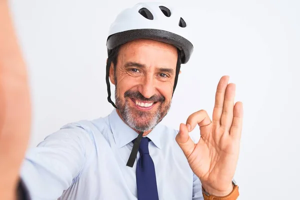 Middle age businessman wearing bike helmet make selfie over isolated white background doing ok sign with fingers, excellent symbol