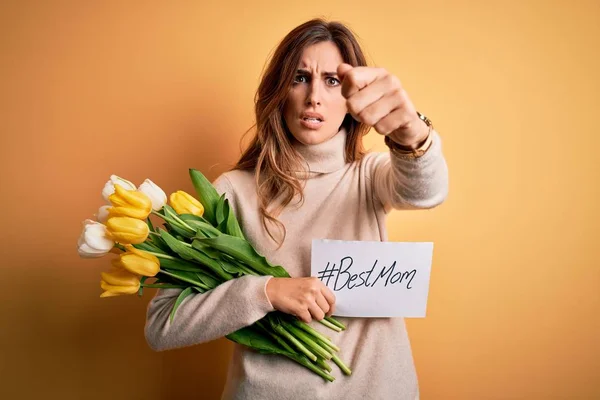 Beautiful brunette woman holding best mom message and tulips celebrating mothers day annoyed and frustrated shouting with anger, crazy and yelling with raised hand, anger concept