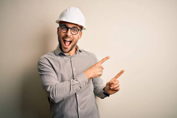 年轻的建筑师头戴建筑商安全帽 背对孤立的背景 微笑着看着摄像机 用双手和手指指向旁边 — 图库照片