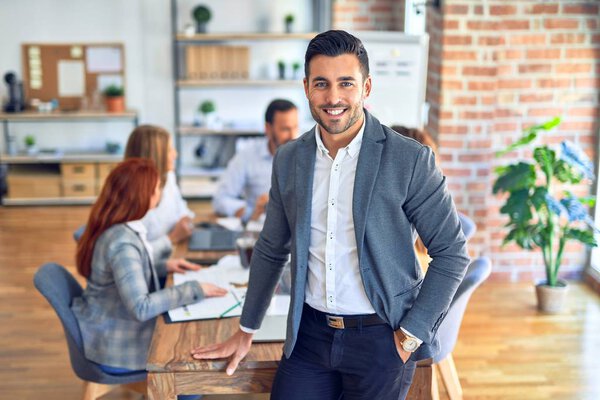 Group of business workers working together. Young handsome businessman standing smiling happy looking at the camera at the office