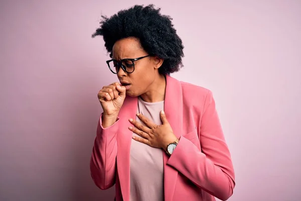 Young beautiful African American afro businesswoman with curly hair wearing pink jacket feeling unwell and coughing as symptom for cold or bronchitis. Health care concept.