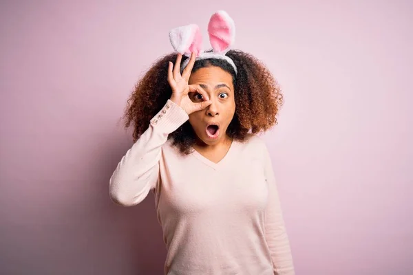 ピンクの背景にウサギの耳を身に着けているアフロの髪を持つ若いアフリカ系アメリカ人女性は 驚きの顔でショックを受けたOkジェスチャーを行い 目は指を見て 不信仰の表現 — ストック写真