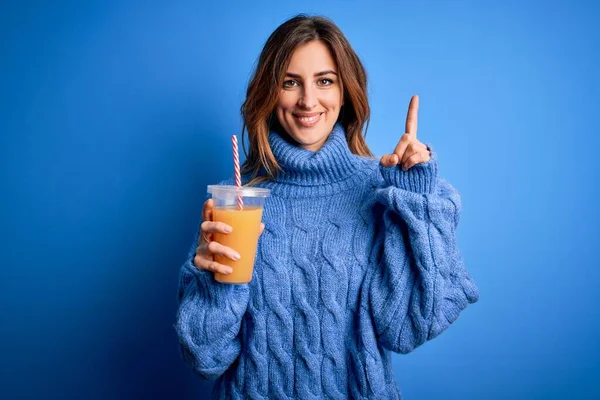 Young Beautiful Brunette Woman Drinking Healthy Orange Juice Blue Background — Stock Photo, Image