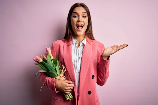 Young beautiful brunette woman holding bouquet of tulips flowers over pink background very happy and excited, winner expression celebrating victory screaming with big smile and raised hands — Stock Image Young Beautiful Brunette Woman Holding Bouquet Tulips Flowers Pink Background Stock Image