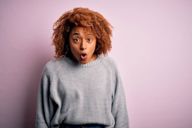 Young beautiful African American afro woman with curly hair wearing casual sweater afraid and shocked with surprise expression, fear and excited face.