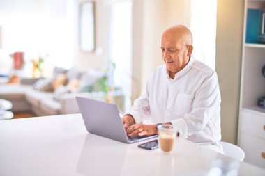 Kıdemli yakışıklı adam mutlu ve kendinden emin gülümsüyor. Evde dizüstü bilgisayar kullanıp kahve içmek.