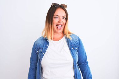 İzole edilmiş beyaz arka planda duran kot gömlekli güzel bir kadın komik bir ifadeyle dilini dışarı çıkartıyor. Duygu kavramı.