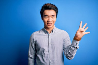 Young handsome chinese man wearing casual shirt standing over isolated blue background showing and pointing up with fingers number four while smiling confident and happy.