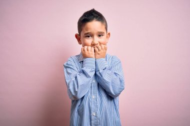 Pembe izole edilmiş arka planda duran zarif tişörtlü genç çocuk elleri ağız yiyen tırnaklarla gergin ve stresli görünüyor. Endişe sorunu.