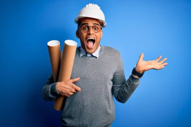 Genç Afro-Amerikan Afro-Amerikan mimar elinde güvenlik kaskı olan mutlu ve heyecanlı bir mimar zaferi büyük bir gülümsemeyle ve el kaldırarak kutluyor.