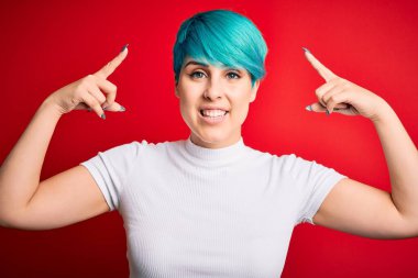 Young beautiful woman with blue fashion hair wearing casual t-shirt over red background smiling pointing to head with both hands finger, great idea or thought, good memory