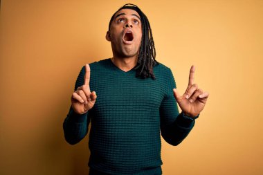 Yeşil günlük kazak giyen Afro-Amerikan Afrikalı genç adam hayrete düştü ve şaşırdı. Parmaklarıyla işaret etti ve kollarını kaldırdı..